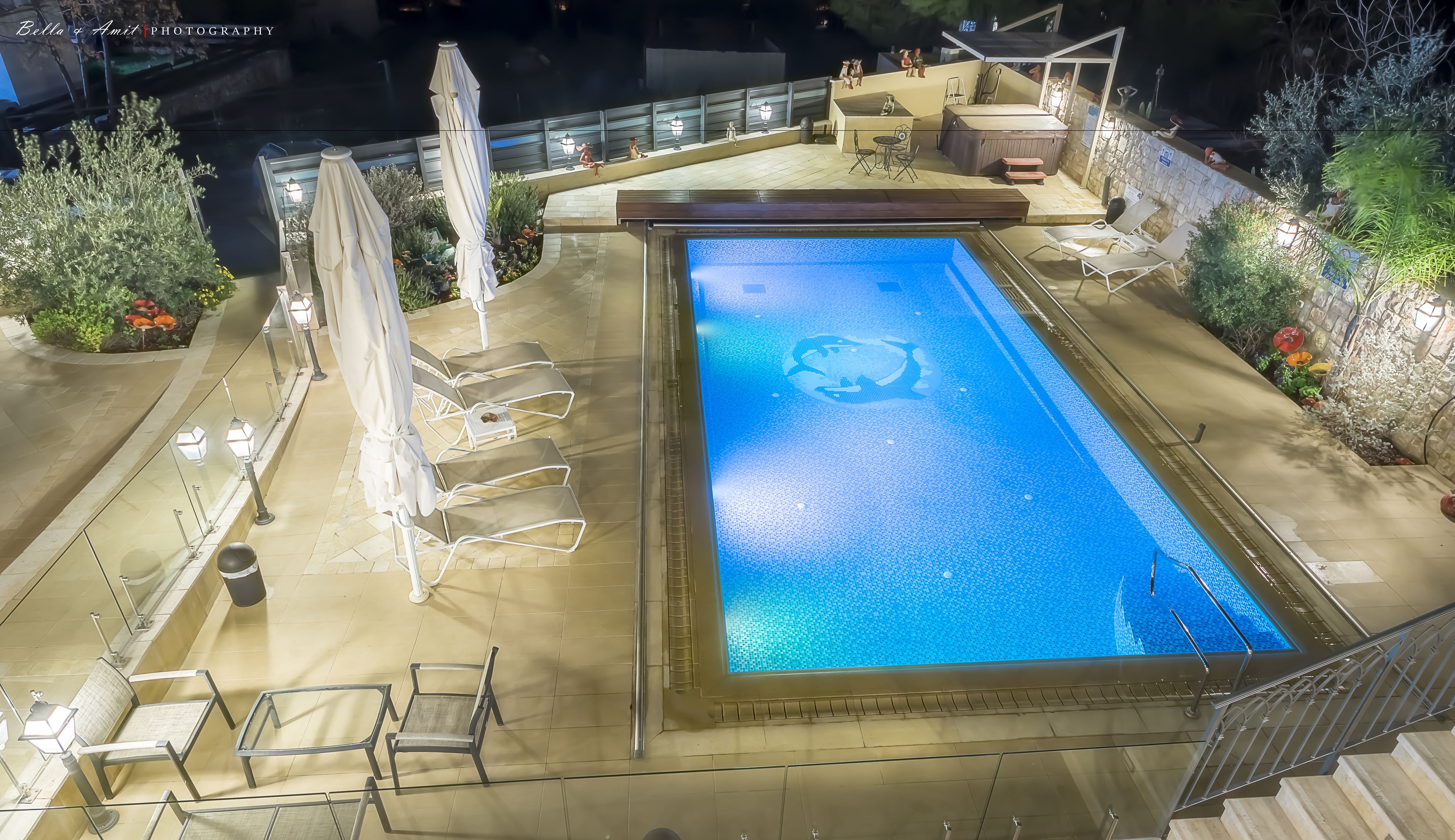 Una piscina con solárium de baldosas, sillas de descanso y zona de hidromasaje.