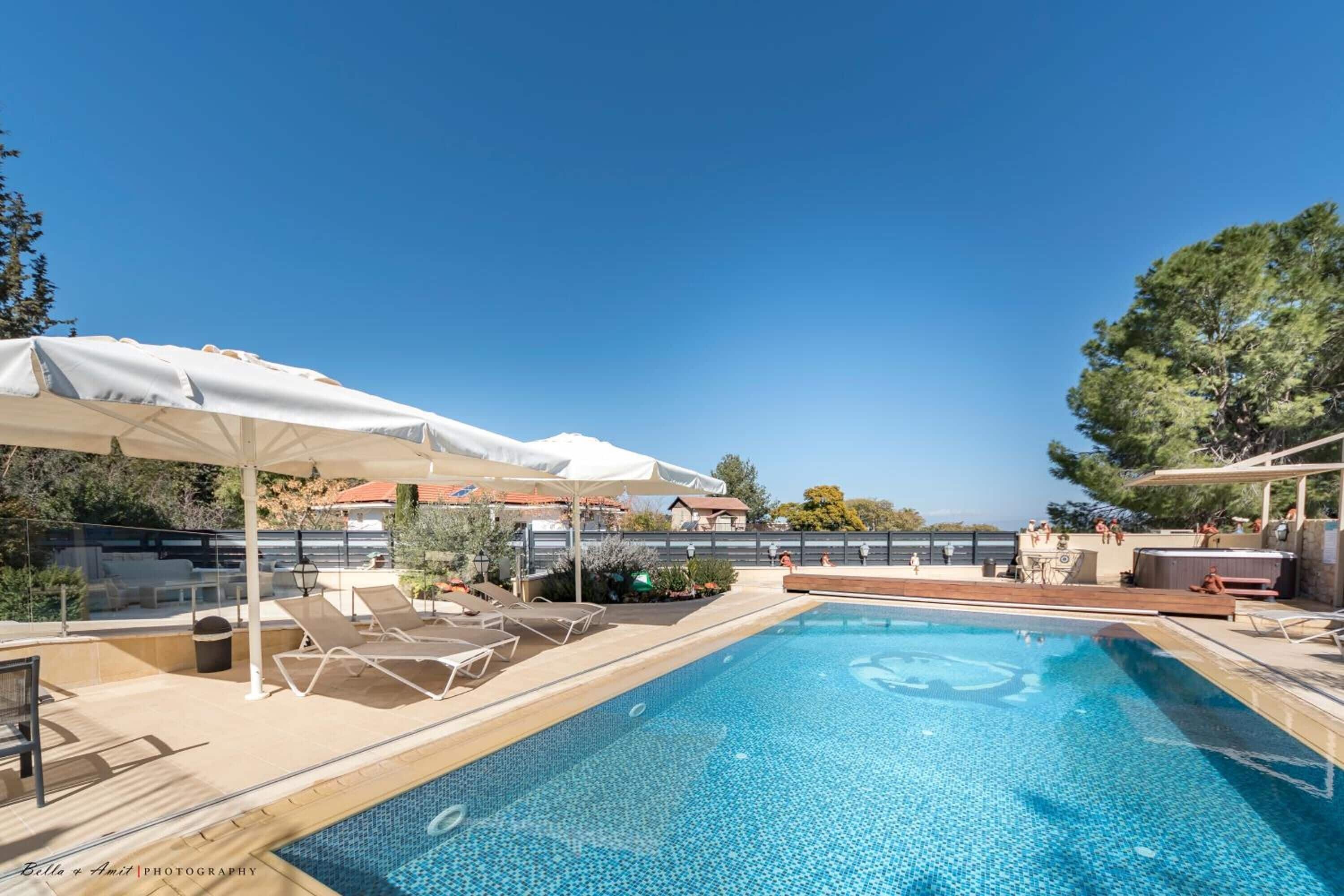 A swimming pool with lounge chairs and umbrellas, surrounded by a deck and trees.