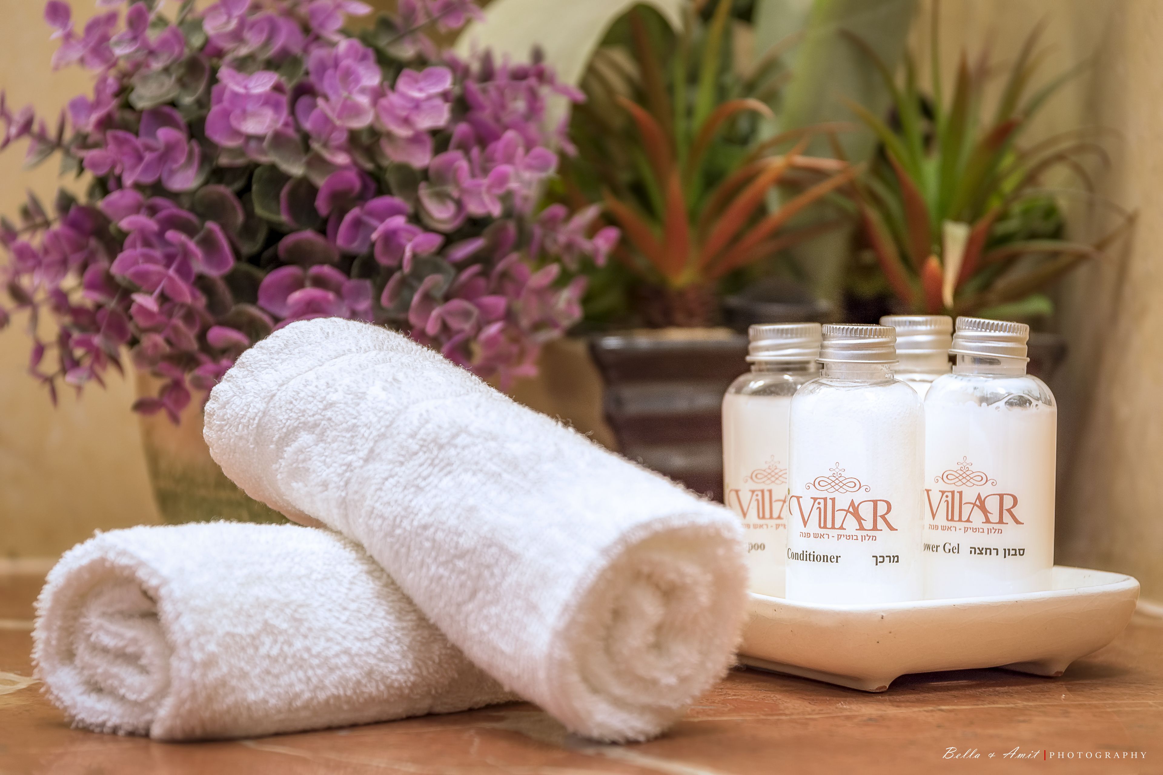 A white towel, three bottles of Vilmar products, and a potted plant with purple flowers.