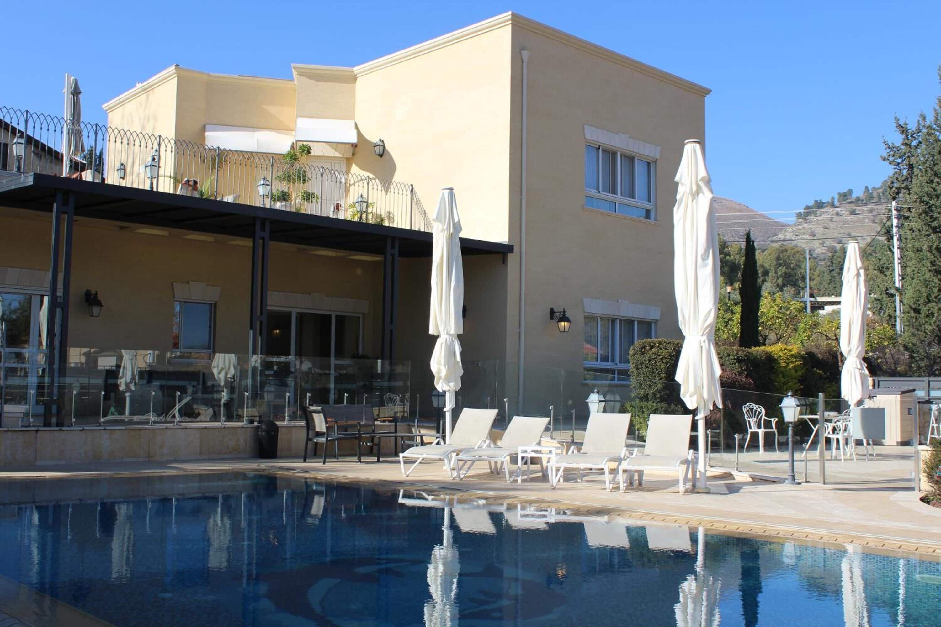 A poolside area with lounge chairs and umbrellas, a building with a balcony, and a clear sky.