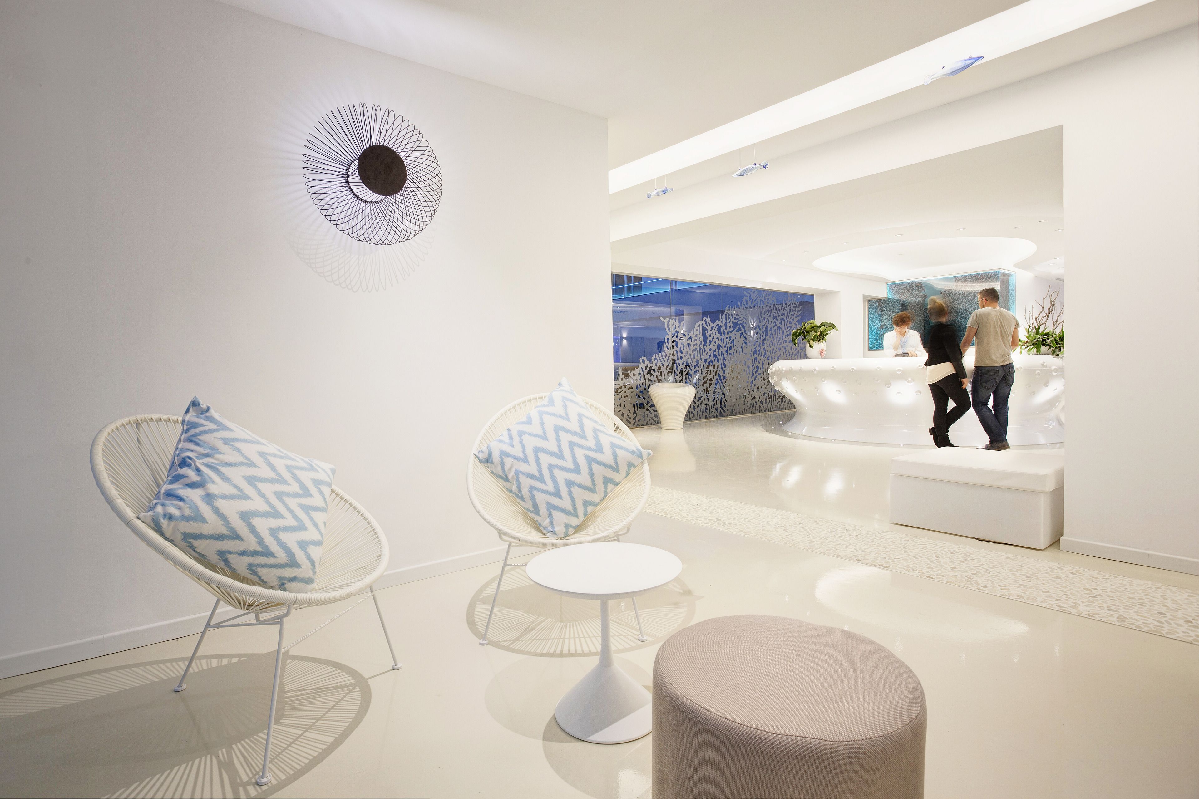 Un lobby moderno con un mostrador de recepción, dos sillones con cojines estampados y un otoman redondo.