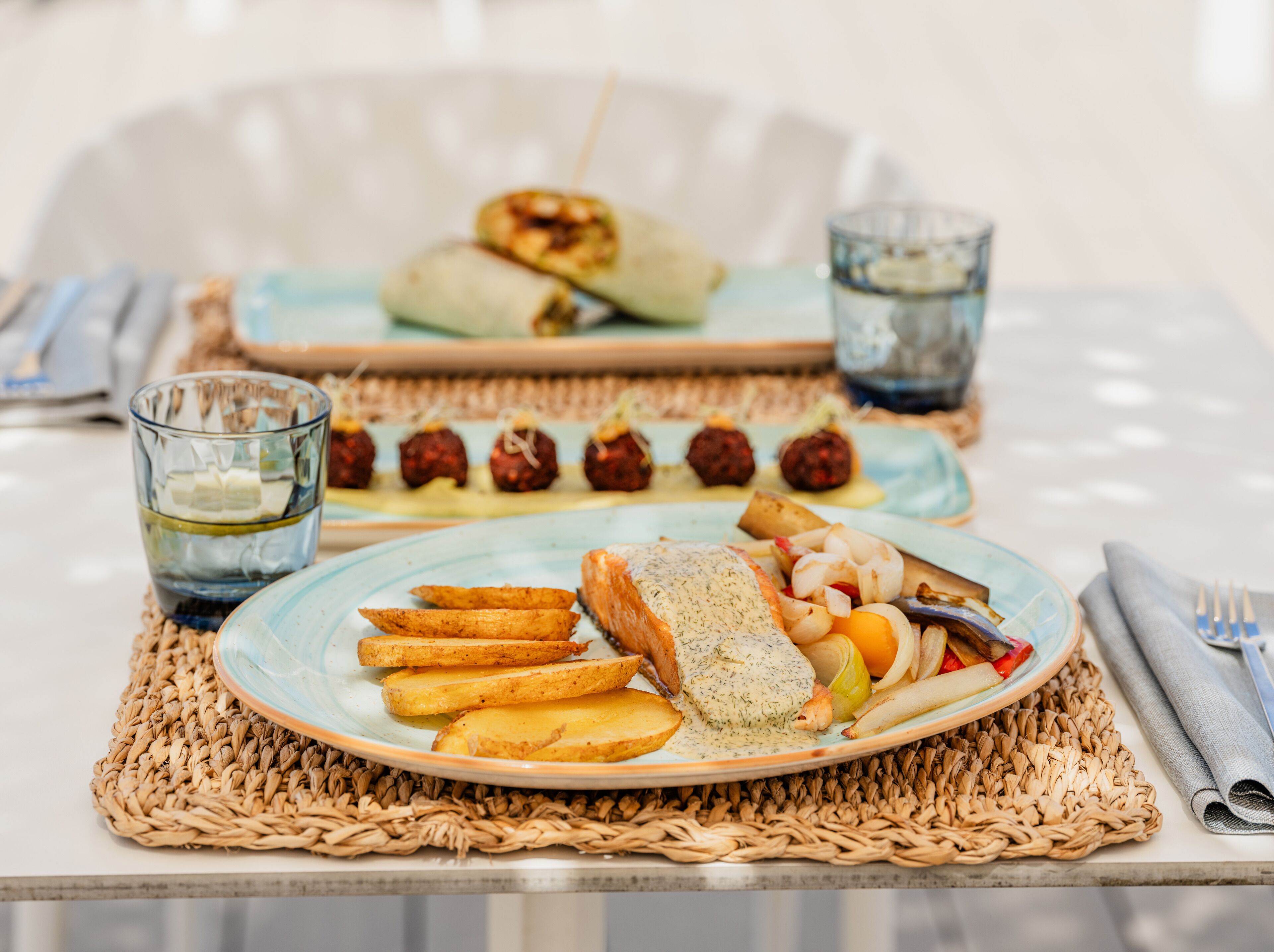 Et bord dækket med mad, herunder fisk, kartofler og grøntsager, samt en tallerken med frikadeller og et glas vand.