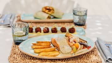 Et bord dækket med mad, herunder fisk, kartofler og grøntsager, samt en tallerken med frikadeller og et glas vand.