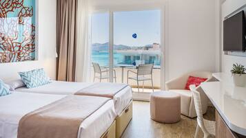 Habitación de hotel con dos camas, un escritorio, una silla, un televisor y un balcón con vista al mar.