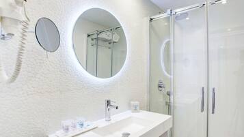 A bathroom with a white sink, a round mirror, and a glass shower enclosure.