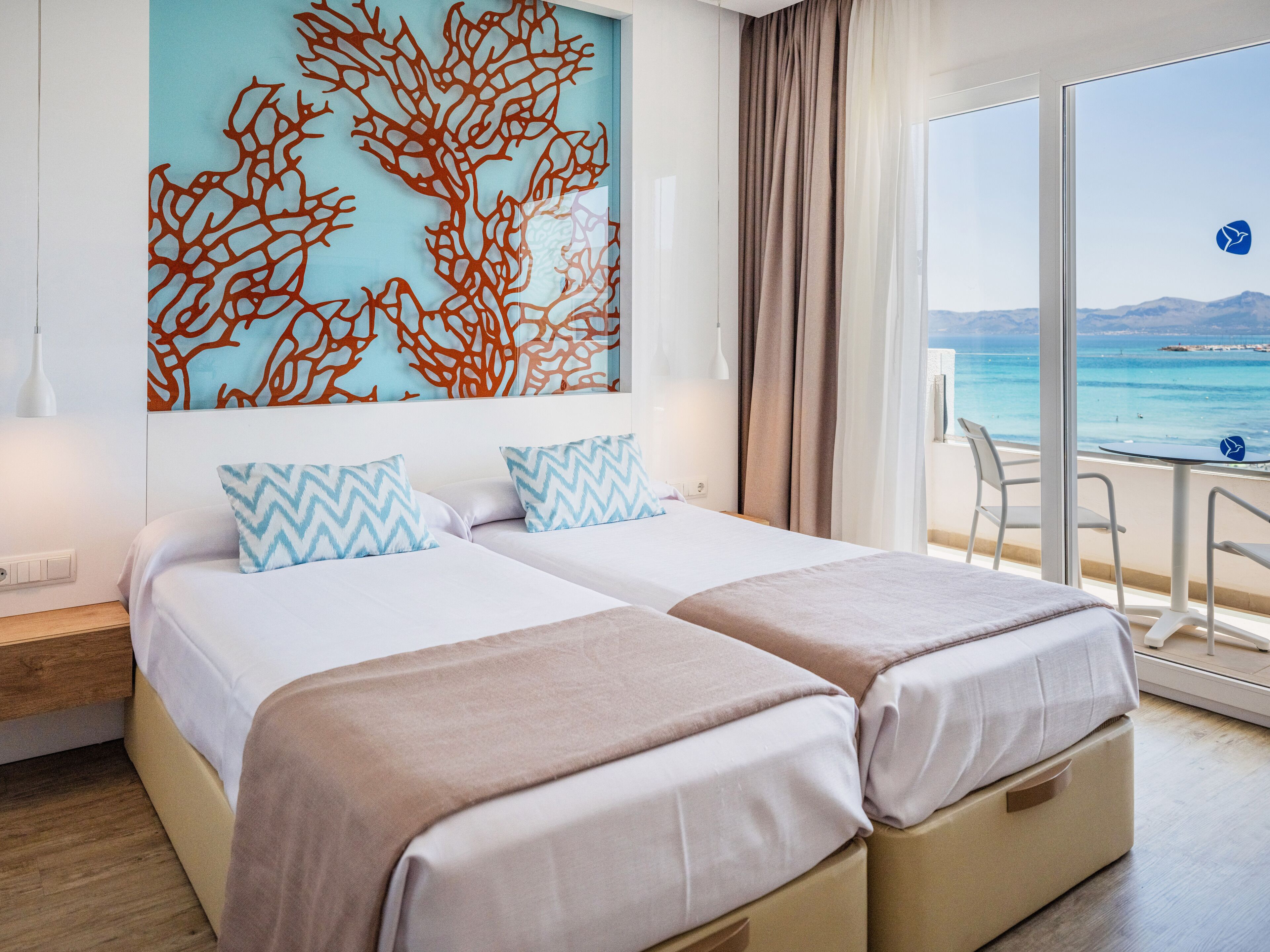Habitación de hotel con dos camas, un ventanal con vistas al mar y una obra de arte decorativa con coral en la pared.