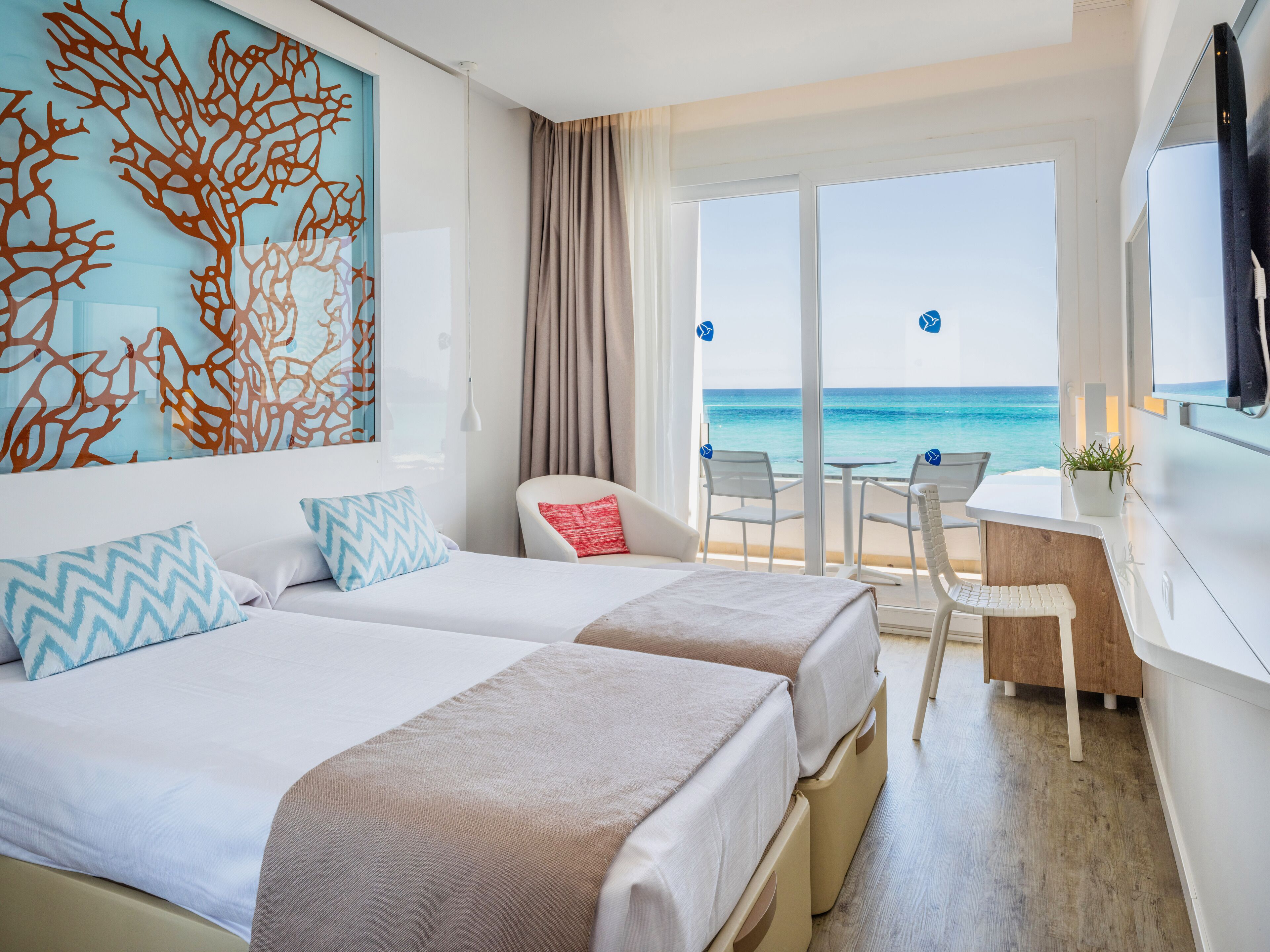 Habitación de hotel con dos camas, un escritorio y vista a la playa.