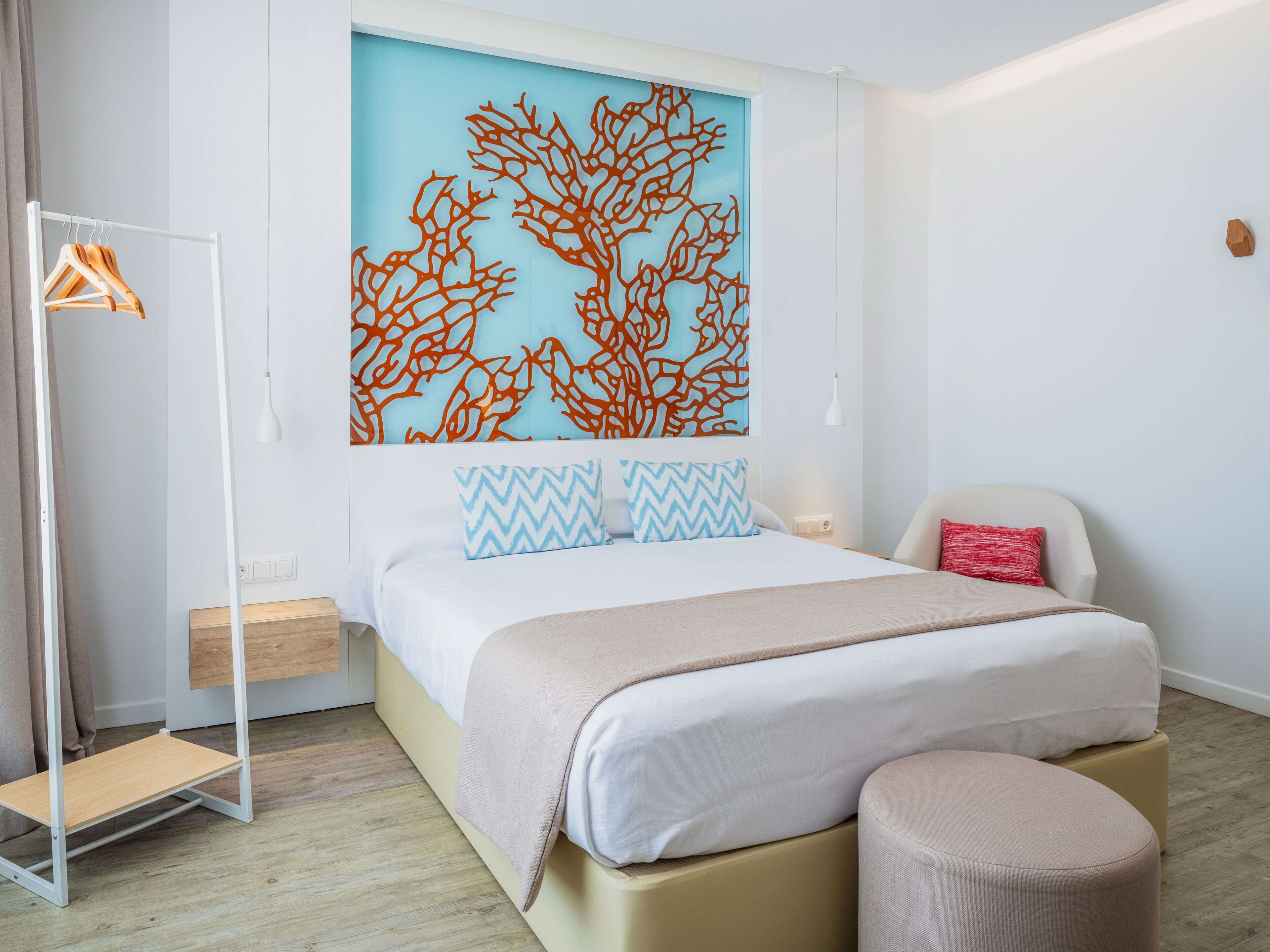 A modern bedroom with a bed, a bedside table, a nightstand, a hanging light, a wardrobe, and a decorative wall piece.