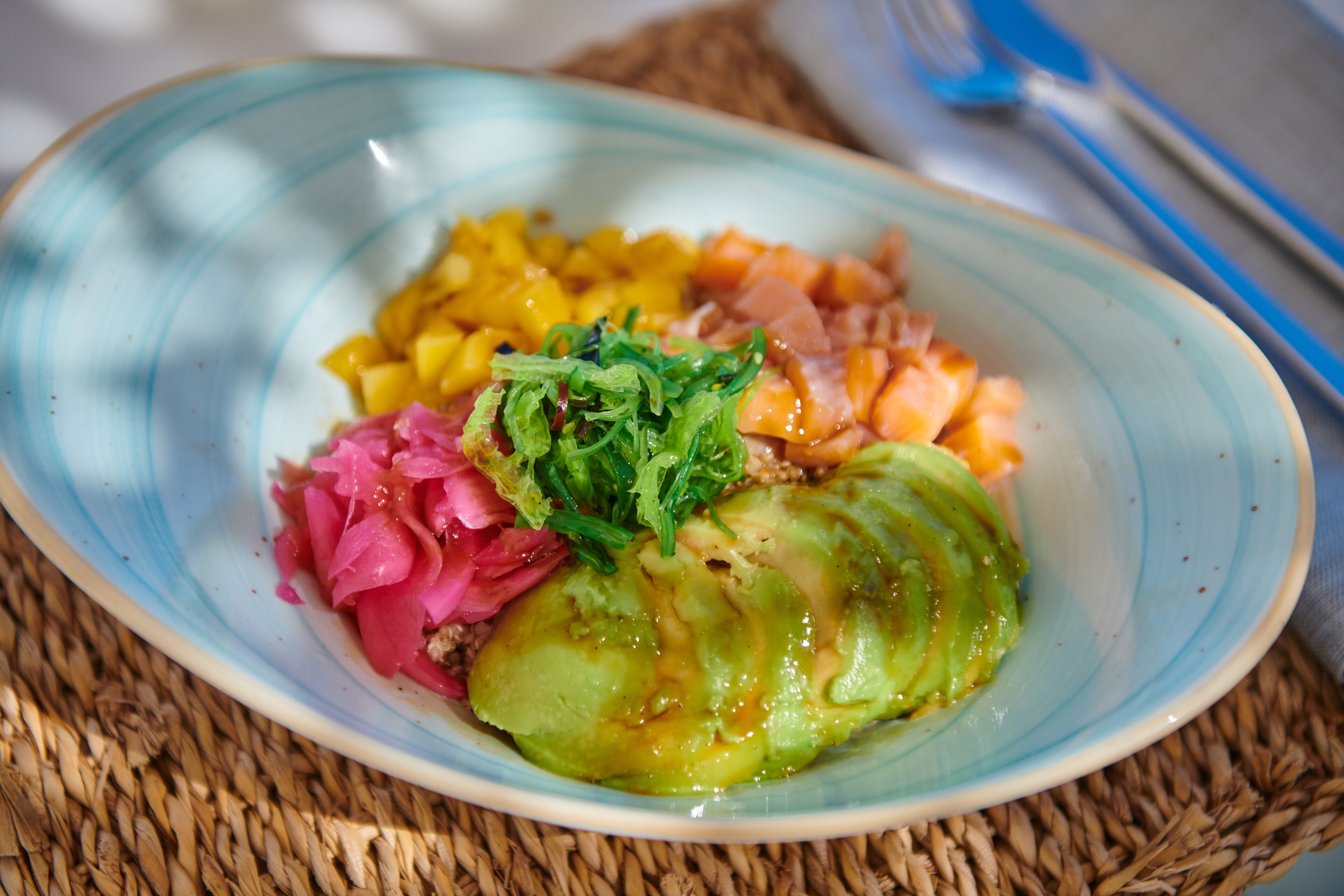 Un plato con diversos alimentos, incluyendo un vegetal verde, fruta amarilla, vegetales encurtidos rosados y una cobertura de hojas verdes.