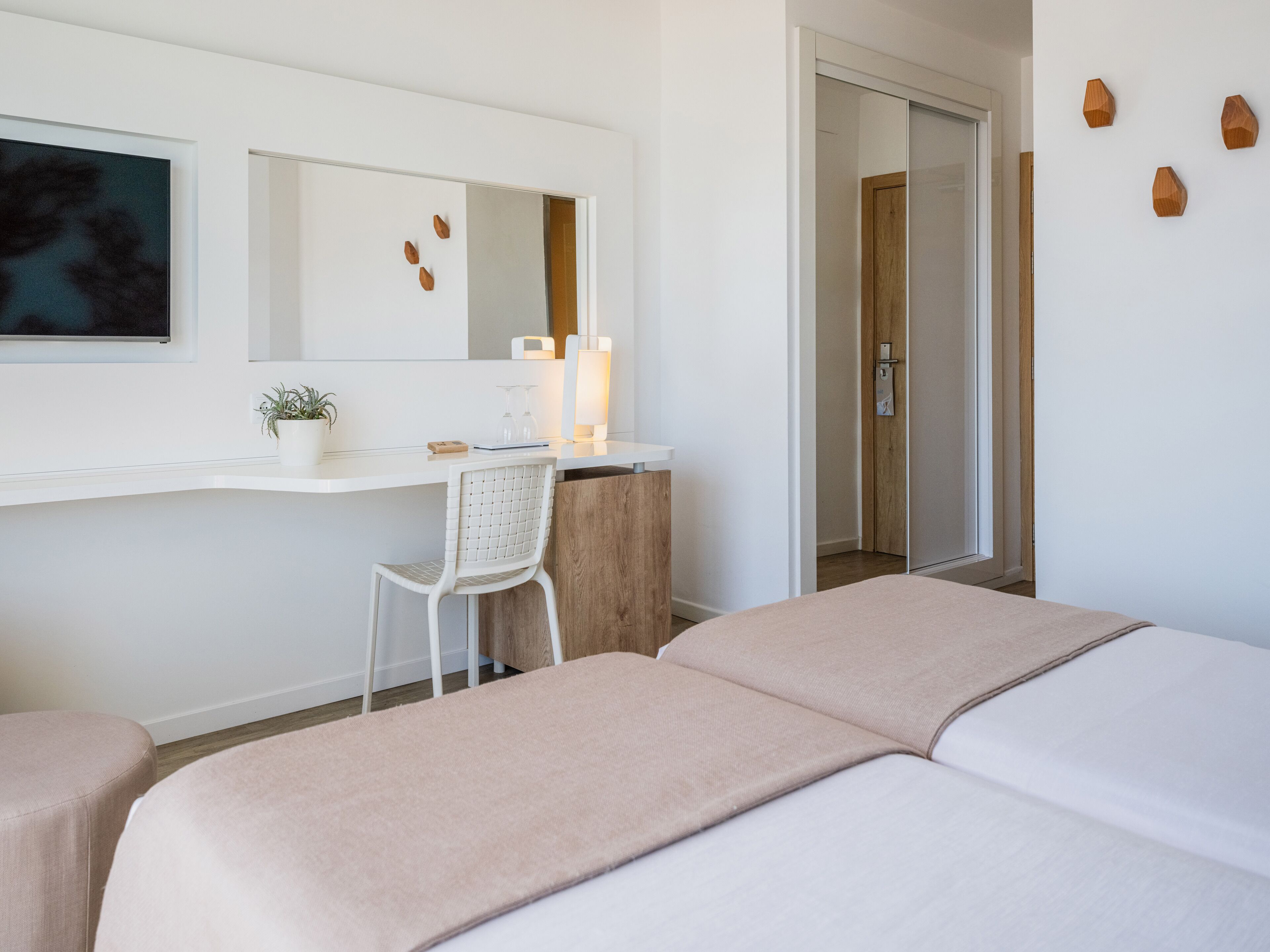 Una habitación de hotel con cama, escritorio, silla, espejo y planta.