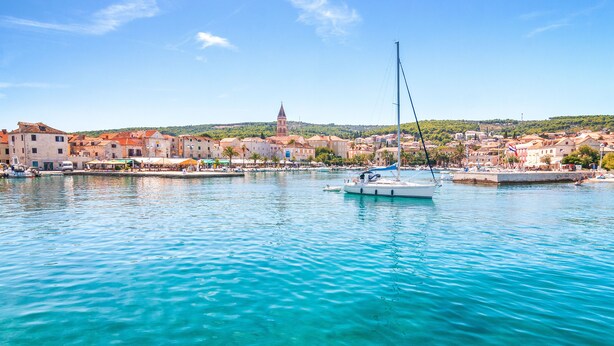 A coastal town with clear turquoise waters, a sailboat, and historic buildings.