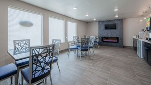 A spacious room with a dining area featuring a table and chairs, a fireplace, and a kitchen area with a TV and appliances. - Stratford House Inns - Edmond (Edmond)