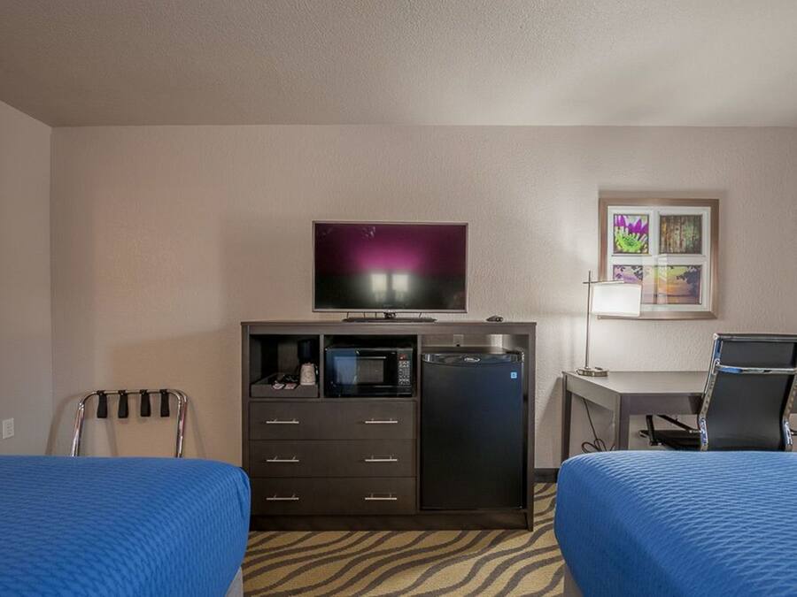 A hotel room with two beds, a TV, a desk, a chair, a microwave, and a refrigerator.