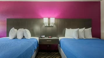 Habitación de hotel con dos camas, cabecera con dos luces empotradas, mesita de noche con un teléfono y un objeto rojo, y alfombra estampada.