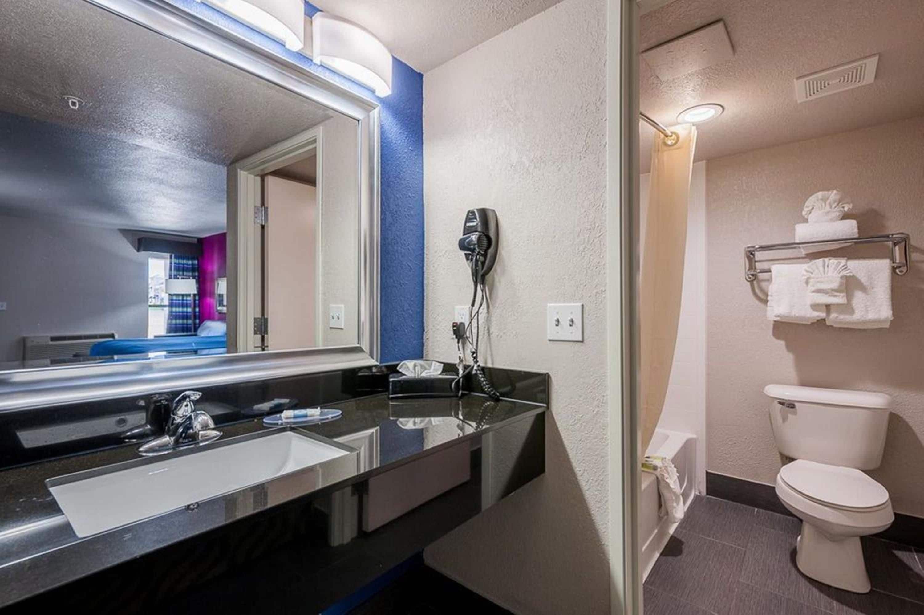 A hotel bathroom with a sink, mirror, hairdryer, and toilet.