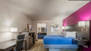 A hotel room with a bed, desk, chair, and a mirror. - Stratford House Inns - Edmond (Edmond)