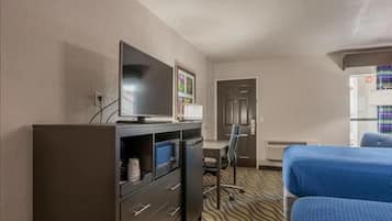 A hotel room with a bed, a desk with a chair, a television on a cabinet, and a door.