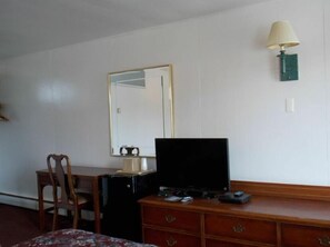 Habitación de hotel con cómoda de madera, televisor, espejo y lámpara de pared.