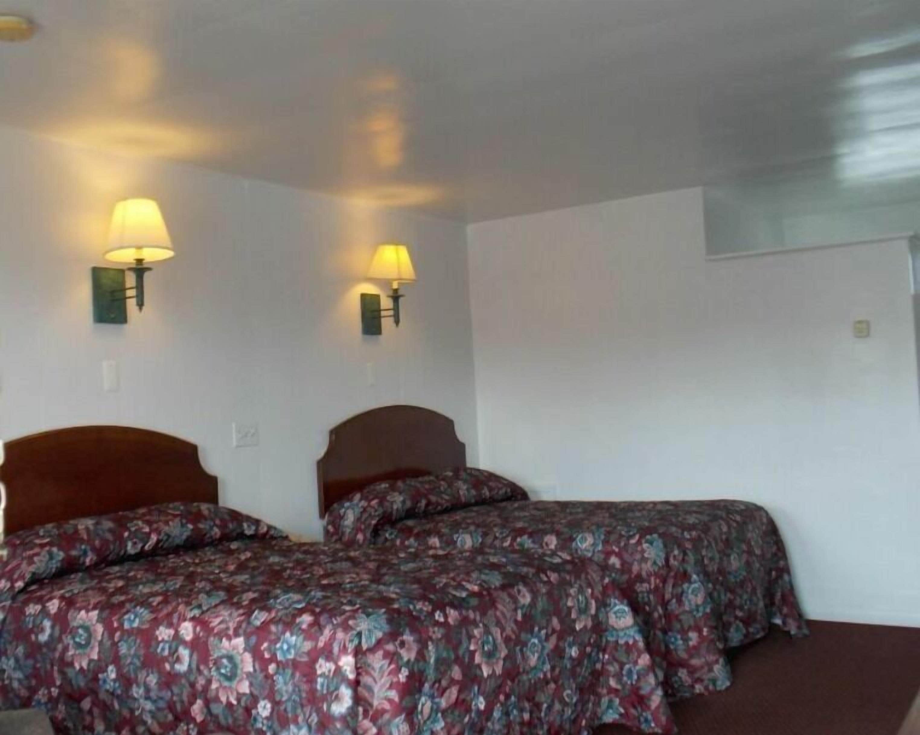 A room with two beds, each with a floral bedspread, two wall-mounted lamps, and a plain white wall.