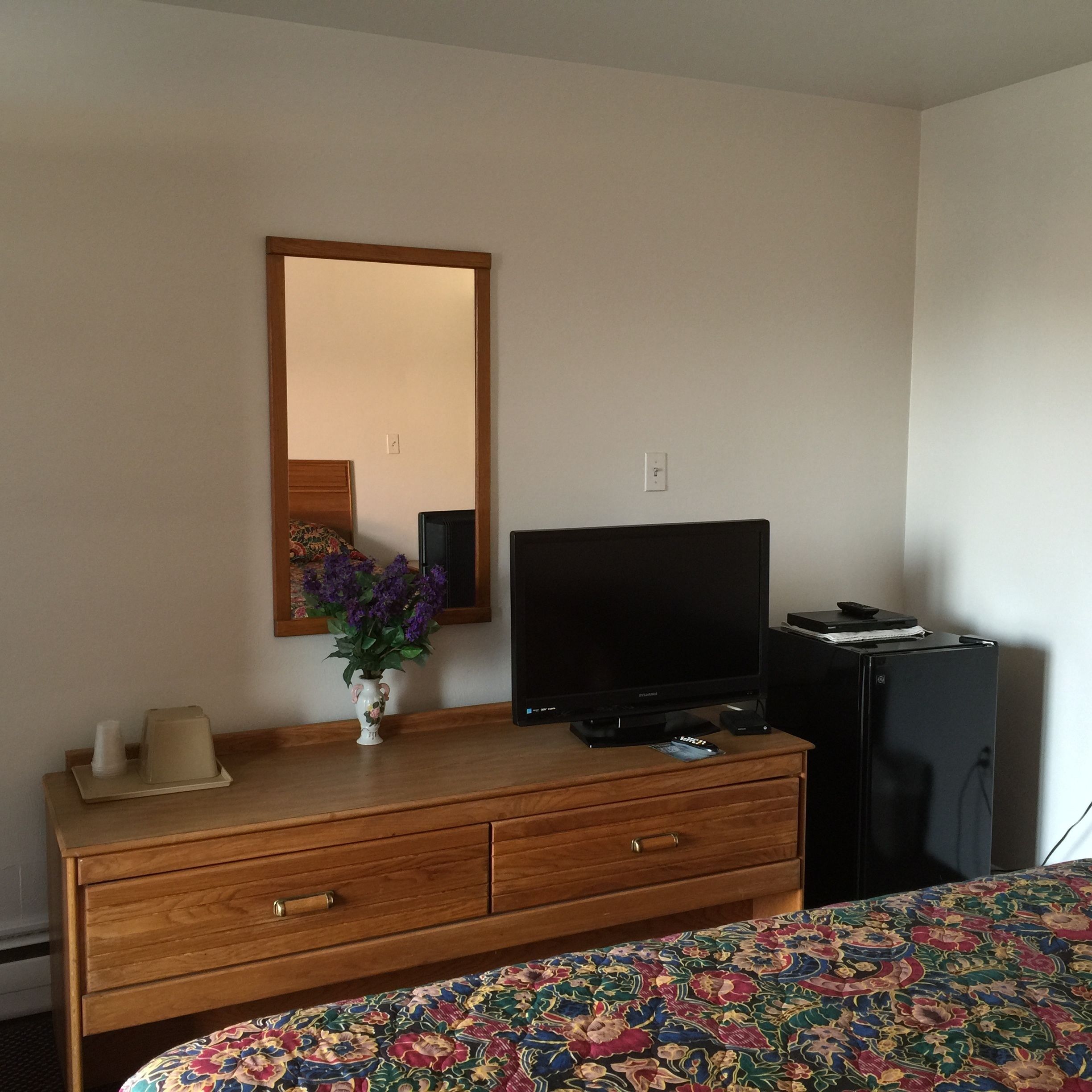 Ein Hotelzimmer mit einem Holzkapfen, einem Fernseher, einem Kühlschrank und einem blumigen Bettüberwurf.