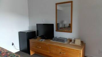 Habitación de hotel con tocador de madera, televisor, espejo y cama con colcha colorida.