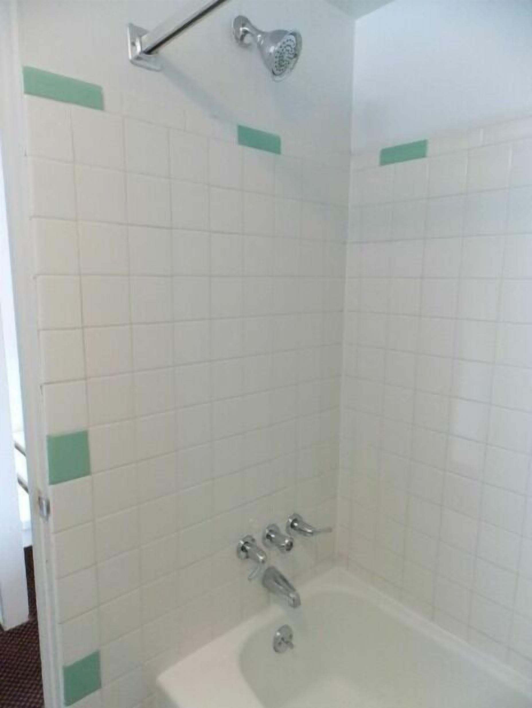 A bathroom with white tiled walls, a bathtub, and a showerhead.