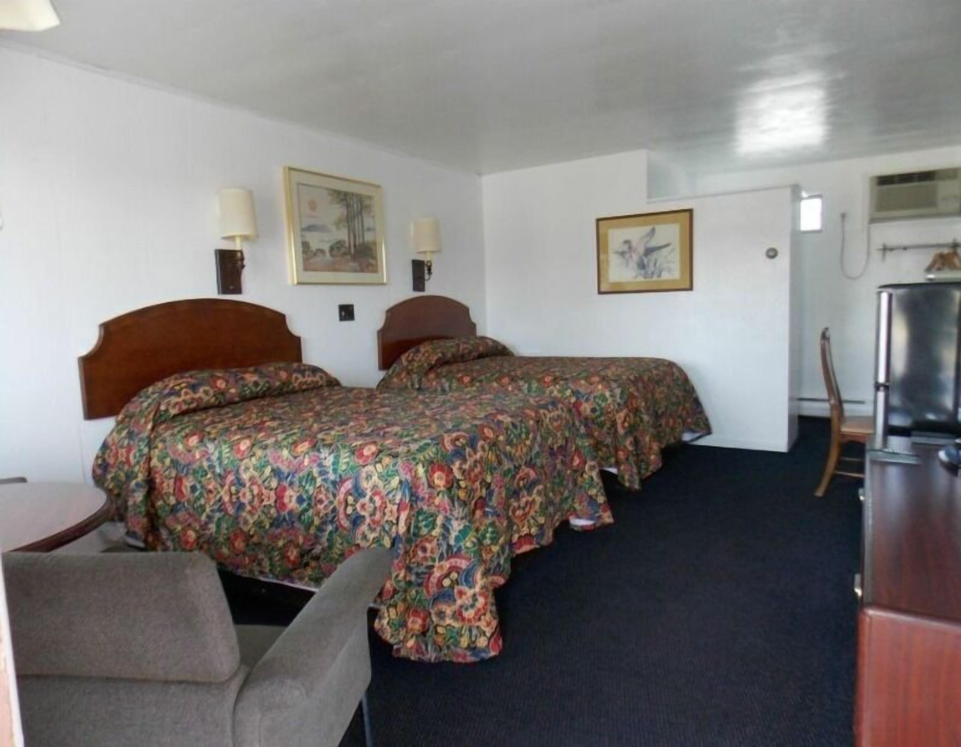A hotel room with two beds, a desk, a chair, and a refrigerator.