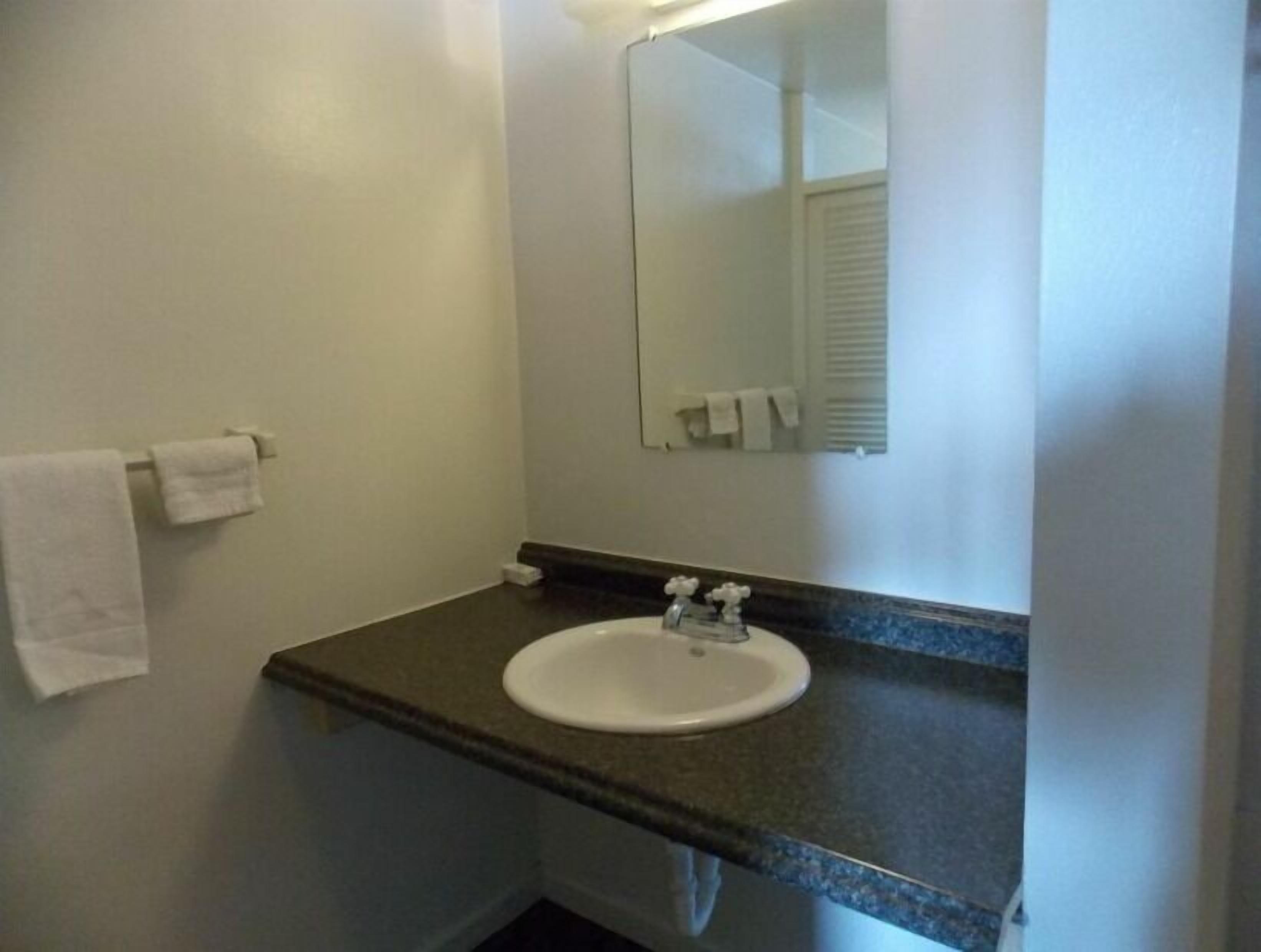 Un baño con un lavamanos blanco, un espejo y una toalla colgada en la pared.