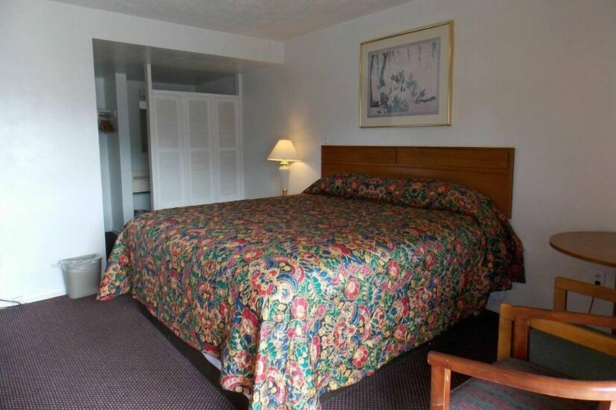 A bedroom with a bed, a chair, a lamp, and a framed picture on the wall.