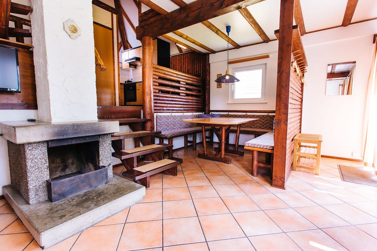 Een rustiek interieur met een stenen openhaard, houten banken en een betegelde vloer.