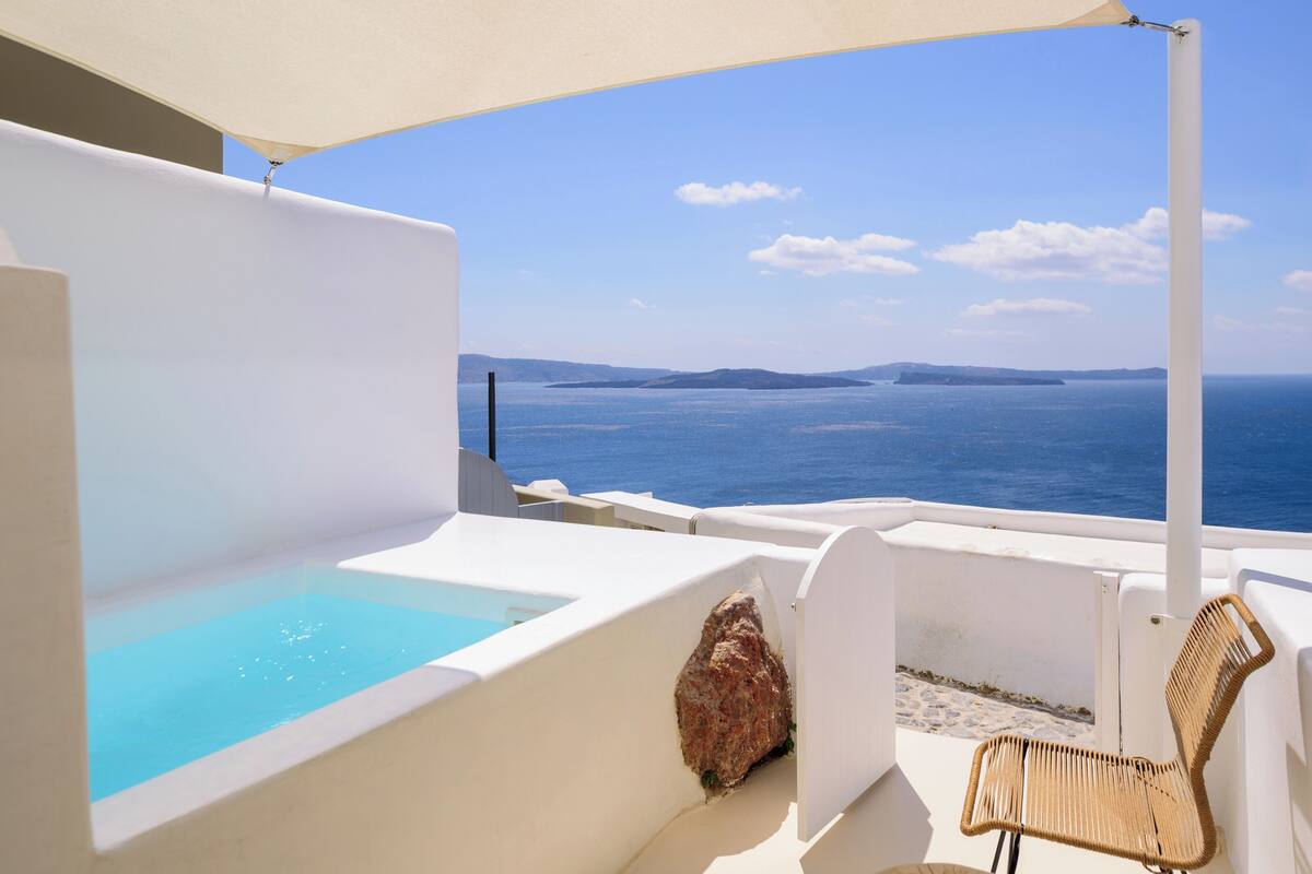 Un balcón con una bañera blanca, una silla de mimbre y vistas al mar.