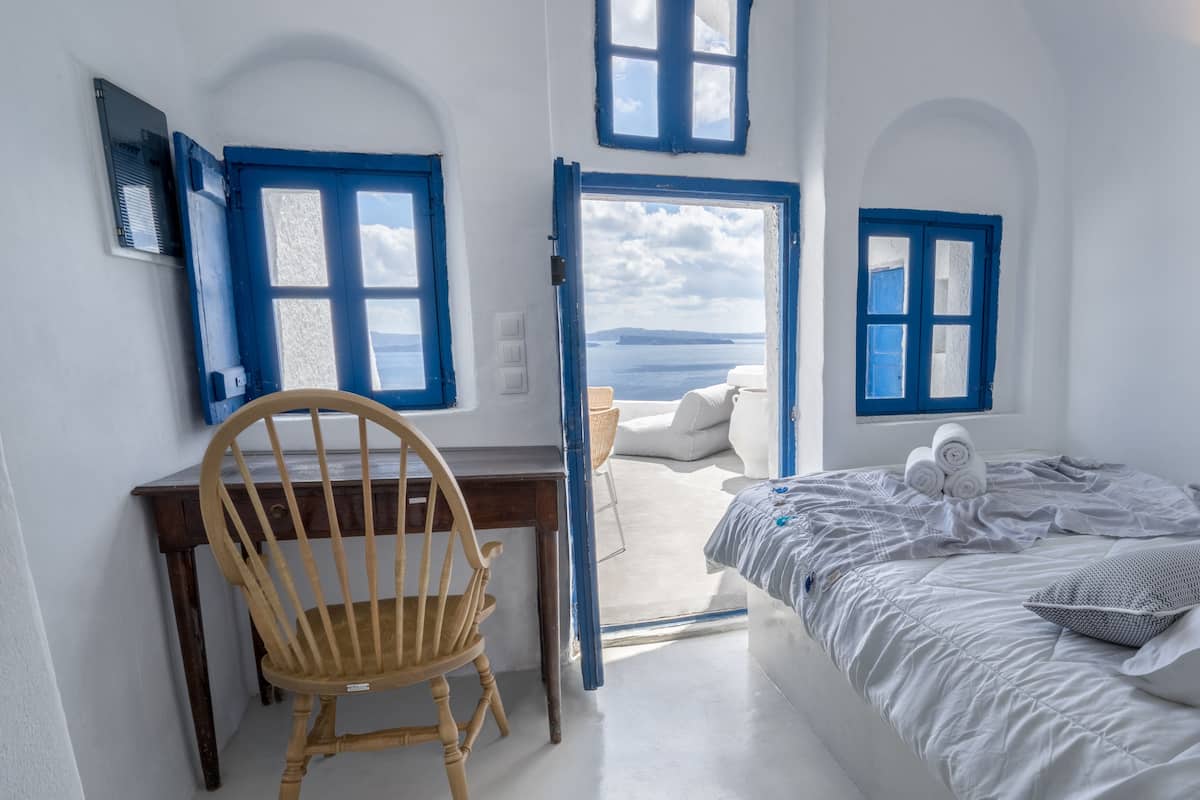 Una habitación con una silla de madera, una cama con toallas enrolladas y vista al mar a través de una puerta.