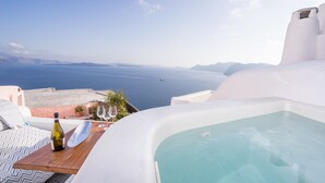 Un espacio exterior lujoso con un jacuzzi, una mesa de madera con una botella y copas, y vistas al mar y montañas a lo lejos.