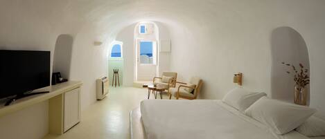 A room with a bed, a TV, a desk, and a chair. There is a window with a view of the sea.