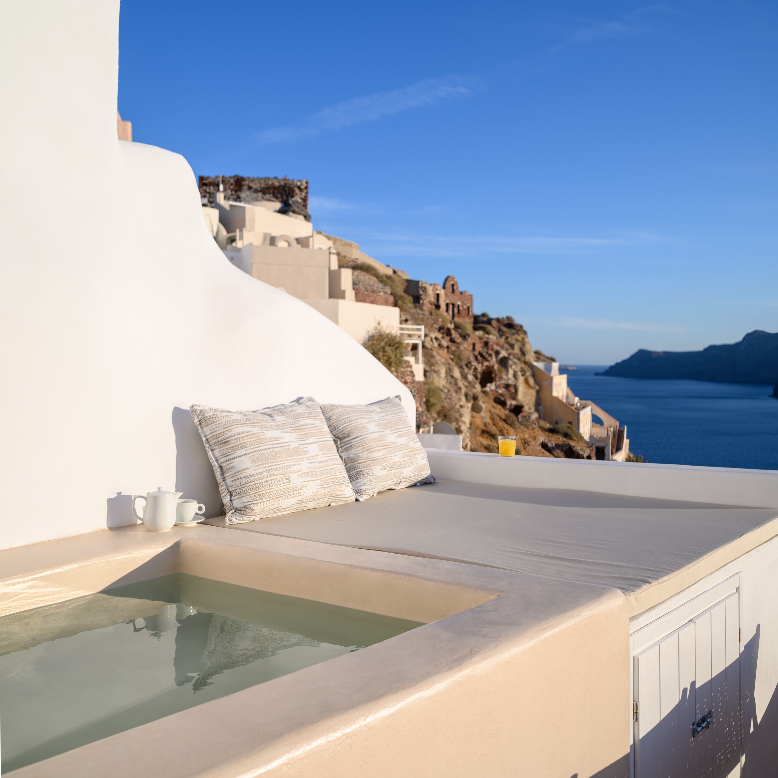 A sunlit terrace with a view of a rocky coastline and the sea.