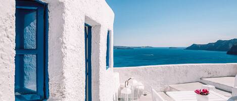 A white building with blue accents, a table with a vase of flowers, and a view of the sea.