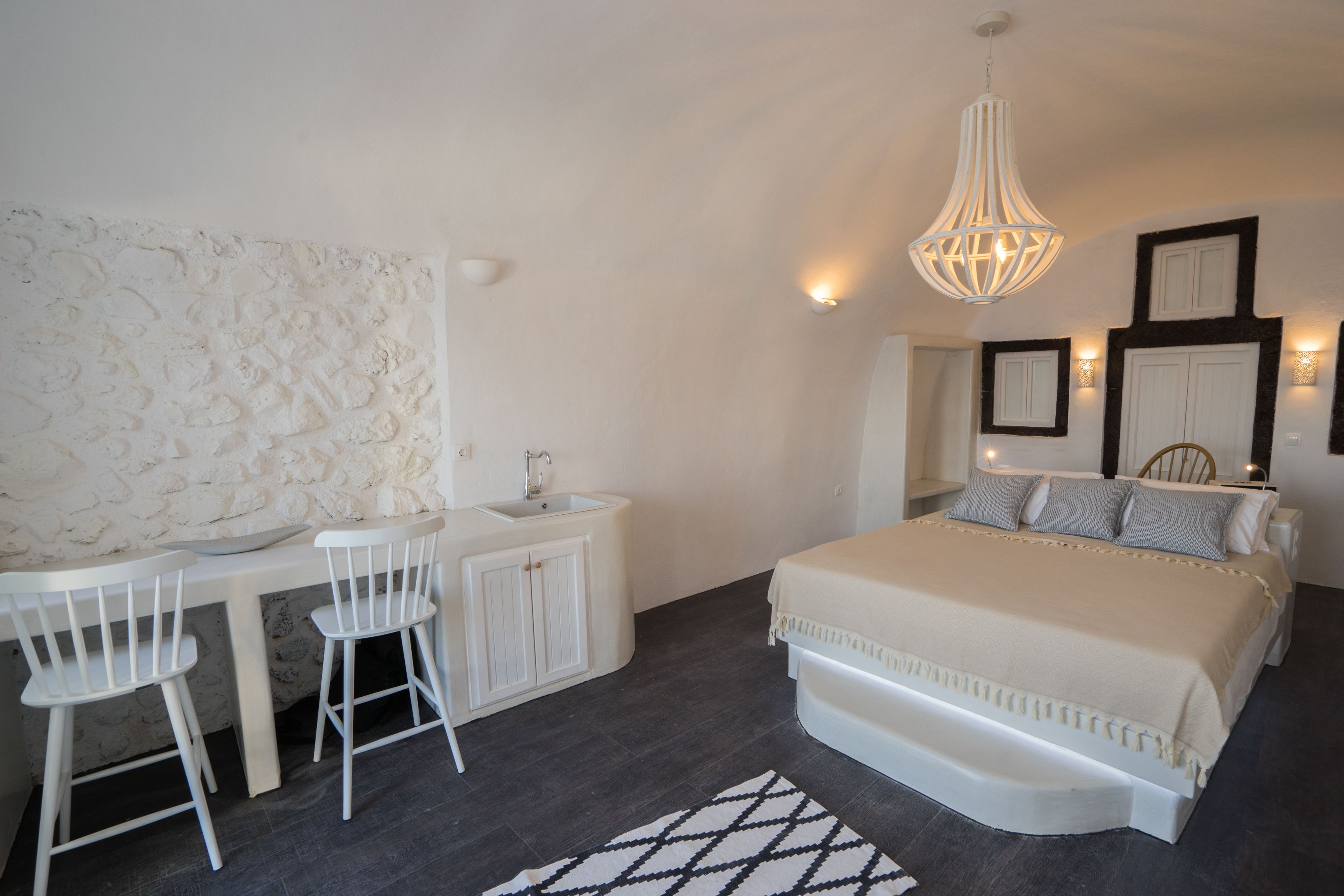 A bedroom with a bed, a desk, two chairs, a sink, and a textured wall.