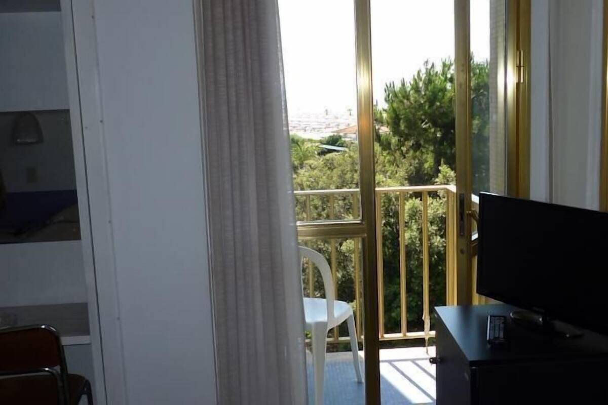 Quarto com televisão em suporte, uma cadeira e varanda com guarda-corpo.