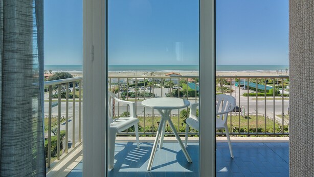 A balcony with a table and chairs, overlooking a beach and a parking area. - Hotel Brasilia (Pietrasanta)