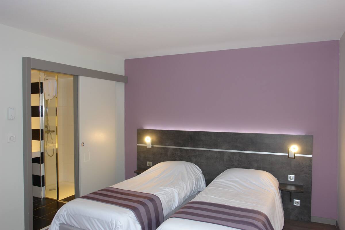Une chambre d’hôtel avec deux lits, un espace douche et un mur de couleur violette.