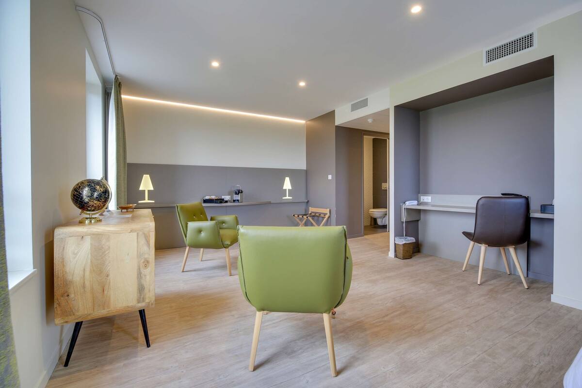 Une chambre d’hôtel moderne avec un bureau en bois, des chaises vertes et un design minimaliste.