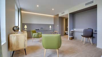 A modern hotel room with a wooden desk, green chairs, and a minimalist design.