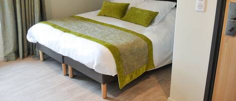 A hotel room with a bed, a bedside table, and a door.