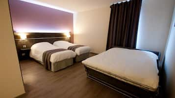 A hotel room with two single beds, a larger bed, wooden flooring, and a headboard with built-in lighting.