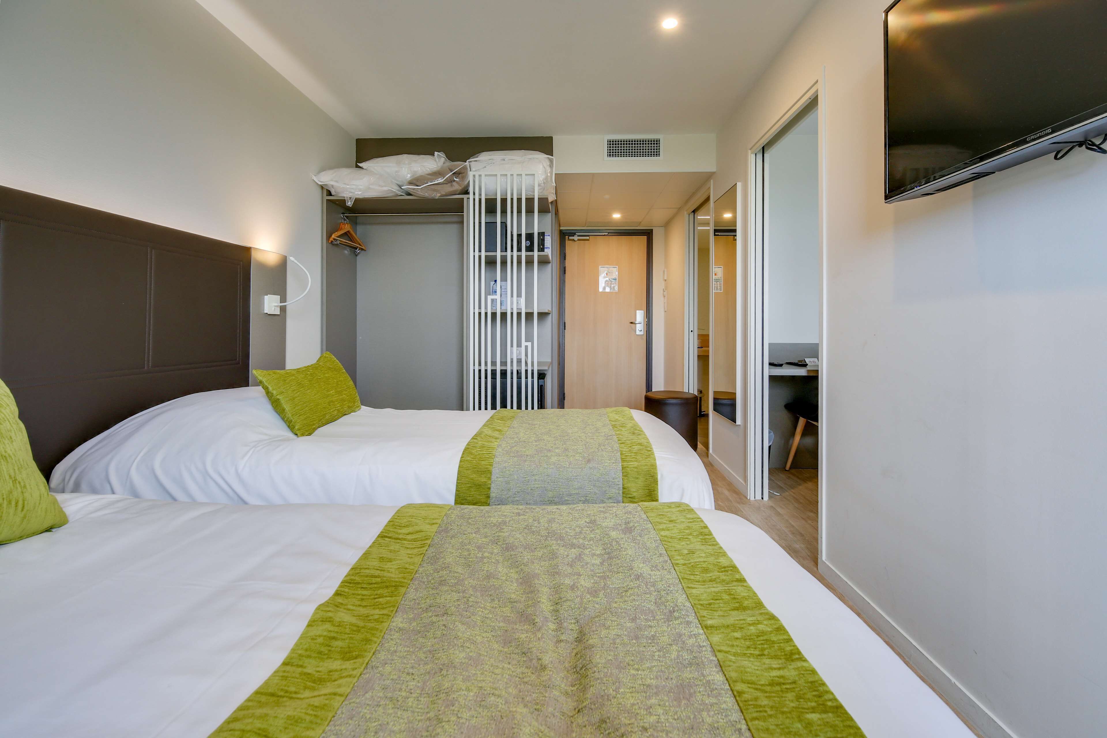 Een hotelkamer met twee bedden, een kledingkast, een televisie en een zichtbare badkamer door een geopende deur.