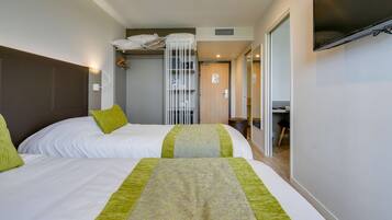 Een hotelkamer met twee bedden, een kledingkast, een televisie en een zichtbare badkamer door een geopende deur.