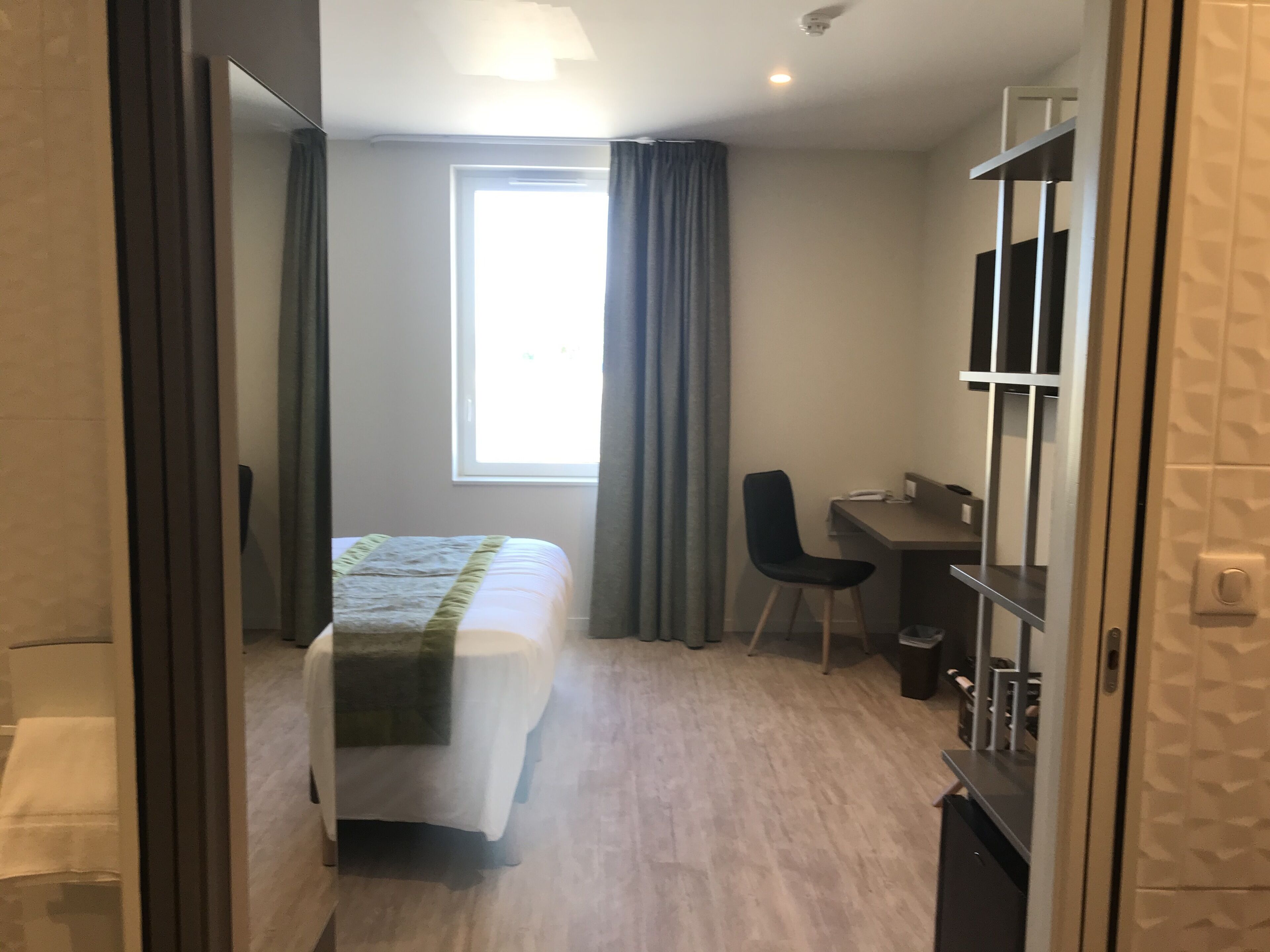 Habitación de hotel con cama, escritorio, silla y un amplio ventanal.