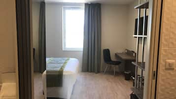 A hotel room with a bed, a desk, a chair, and a large window.