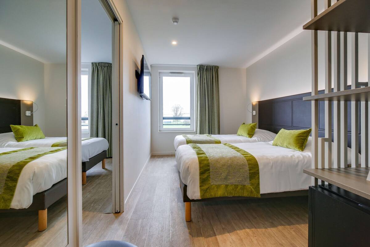 Une chambre d’hôtel avec deux lits, une télévision, un bureau et une fenêtre avec des rideaux.