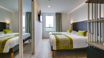 A hotel room with two beds, a television, a desk, and a window with curtains.